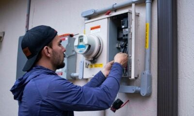 A person in a blue hoodie and baseball cap working on an electrical meter