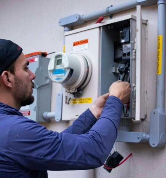 A person in a blue hoodie and baseball cap working on an electrical meter