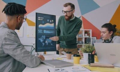 A man pointing at a vertical monitor displaying data charts to two colleagues