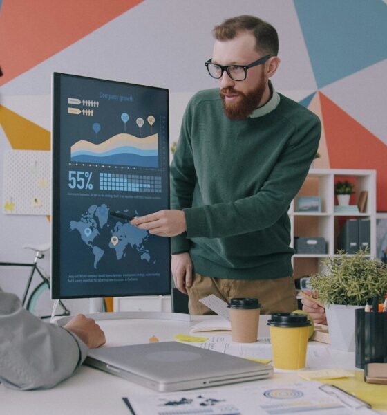 A man pointing at a vertical monitor displaying data charts to two colleagues