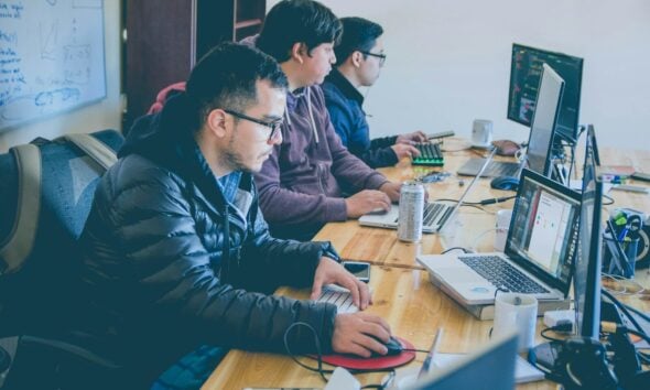 three men facing computer monitors