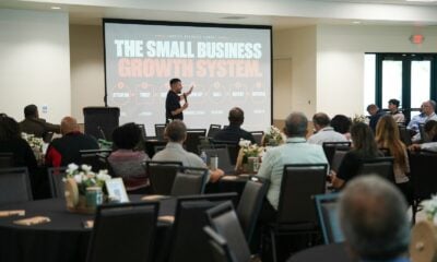 A speaker presenting to an audience in a conference room with a large screen