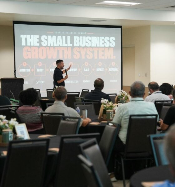 A speaker presenting to an audience in a conference room with a large screen