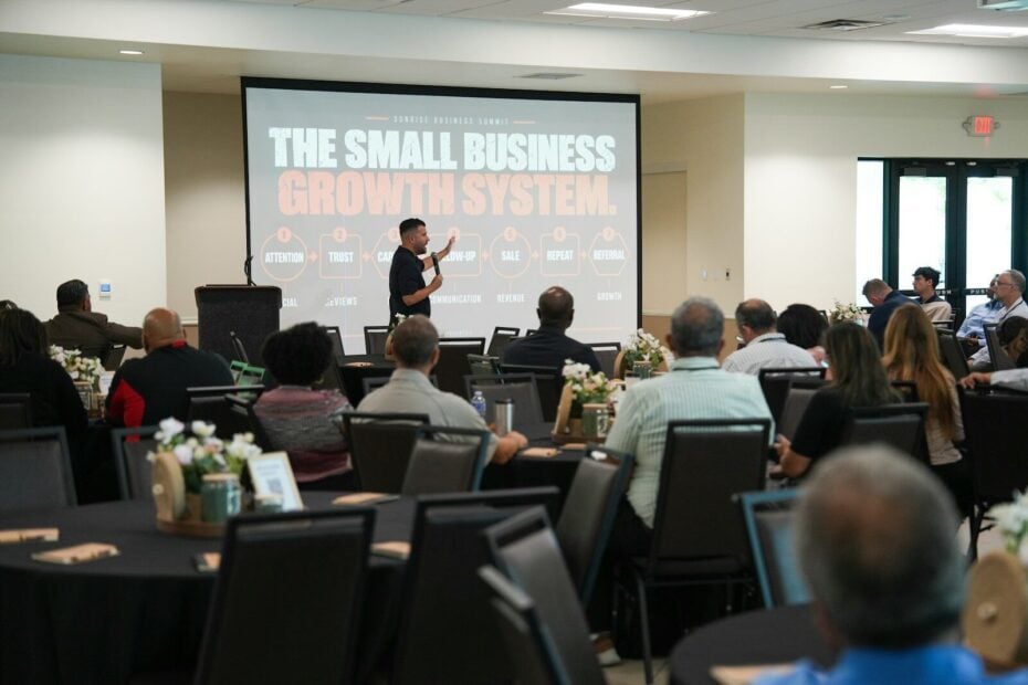 A speaker presenting to an audience in a conference room with a large screen