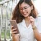 A woman in a white shirt laughing while looking at her smartphone