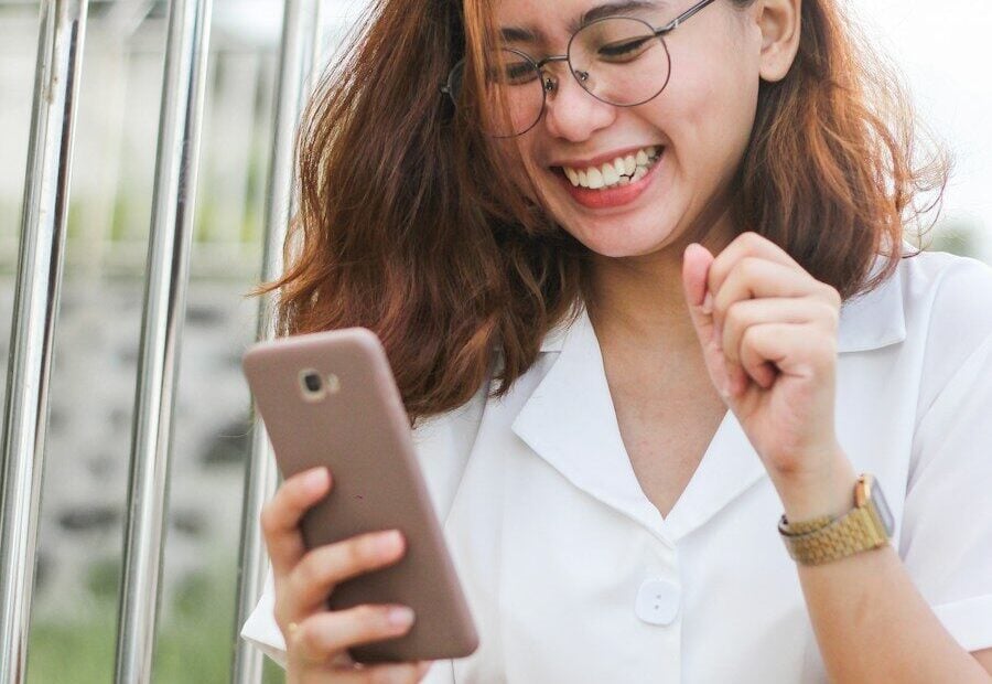 A woman in a white shirt laughing while looking at her smartphone
