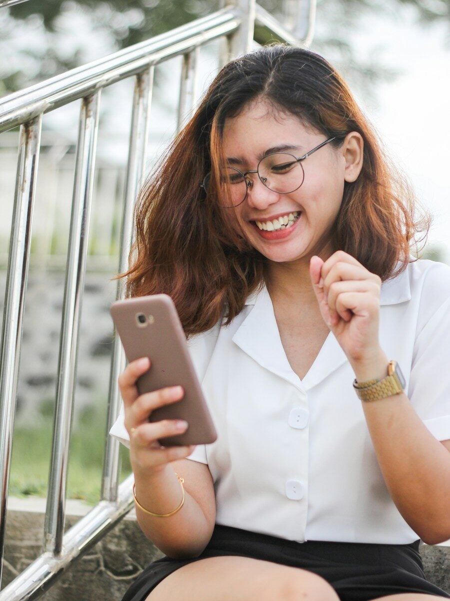 A woman in a white shirt laughing while looking at her smartphone