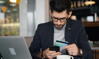 a man sitting at a table looking at his cell phone and holding a credit card