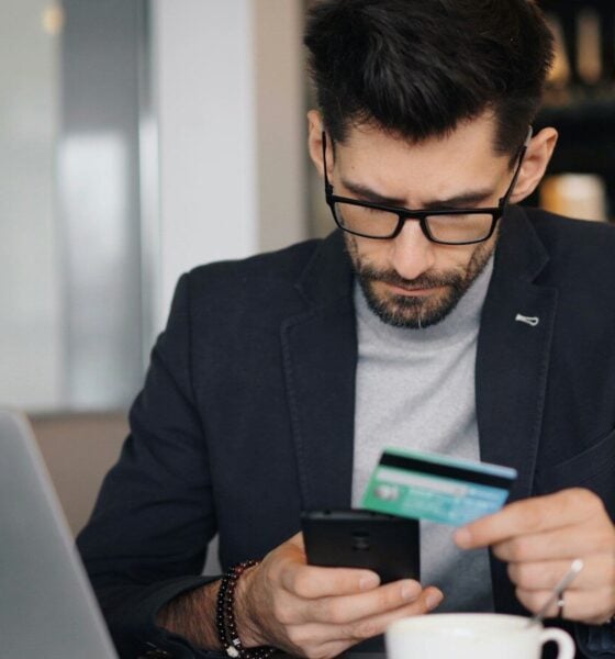 a man sitting at a table looking at his cell phone and holding a credit card