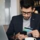 a man sitting at a table looking at his cell phone and holding a credit card