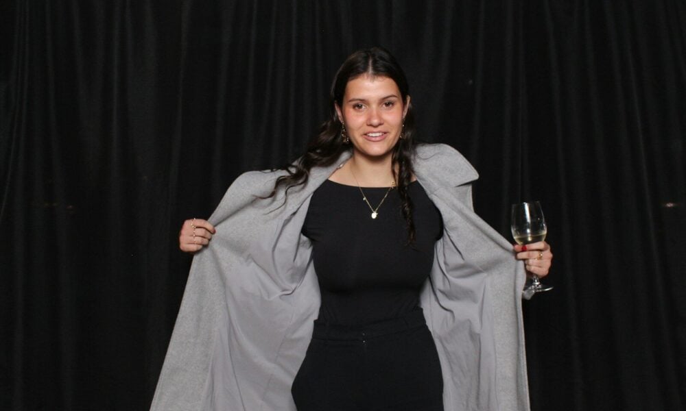 A woman holding a glass of wine in front of a black backdrop